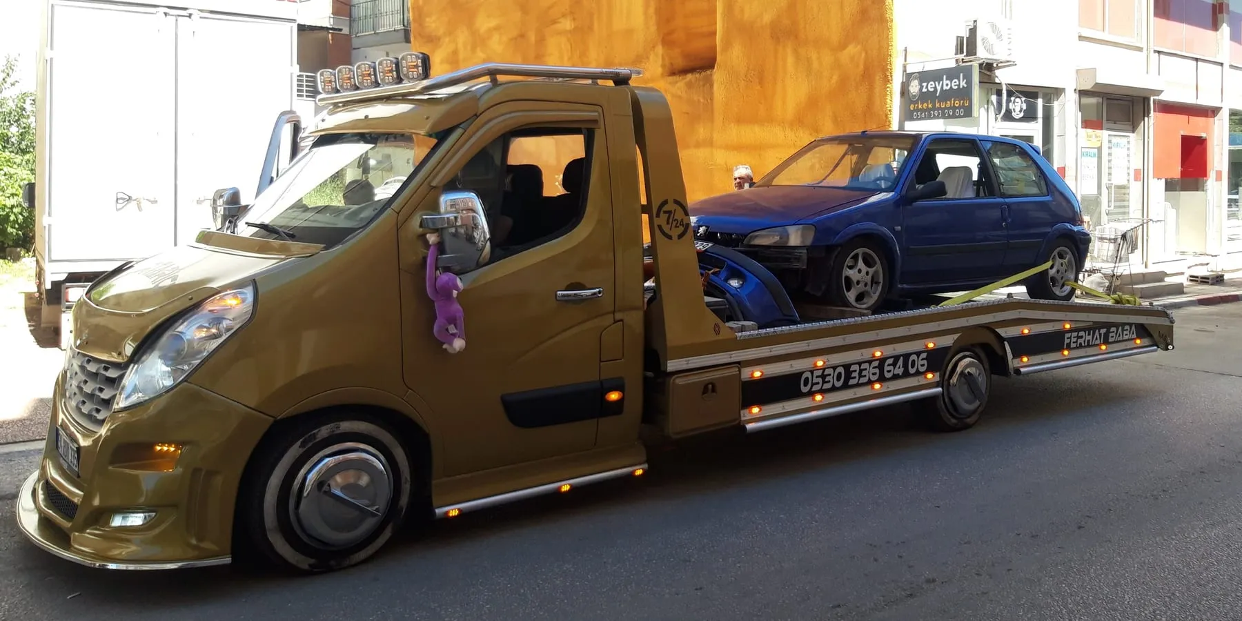 Yanında FERHAT BABA yazısı ve 0530 336 64 06 numarası bulunan sabit kasa çekici, platformunda otomobille — gündüz yan görünüm